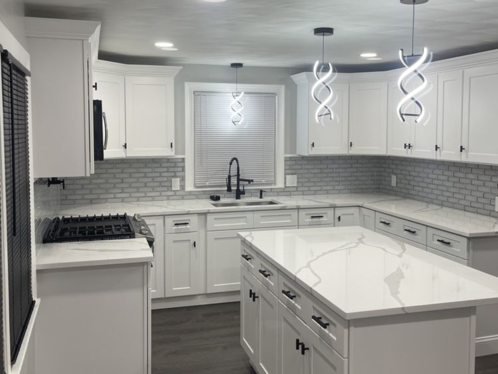 View of a custom kitchen design featuring a white quartz island, gray subway tile backsplash, and modern spiral pendant lights.