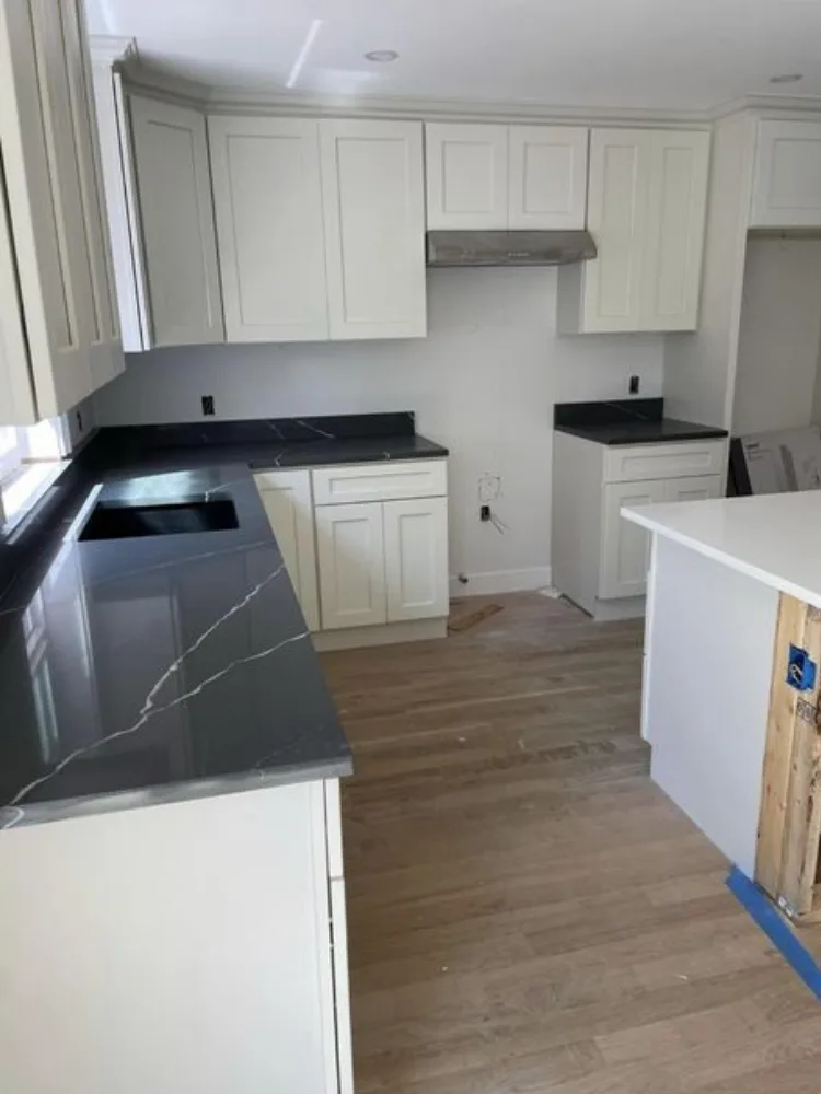 Professional installation of custom kitchen cabinetry featuring white shaker doors and dark marbled quartz countertops.