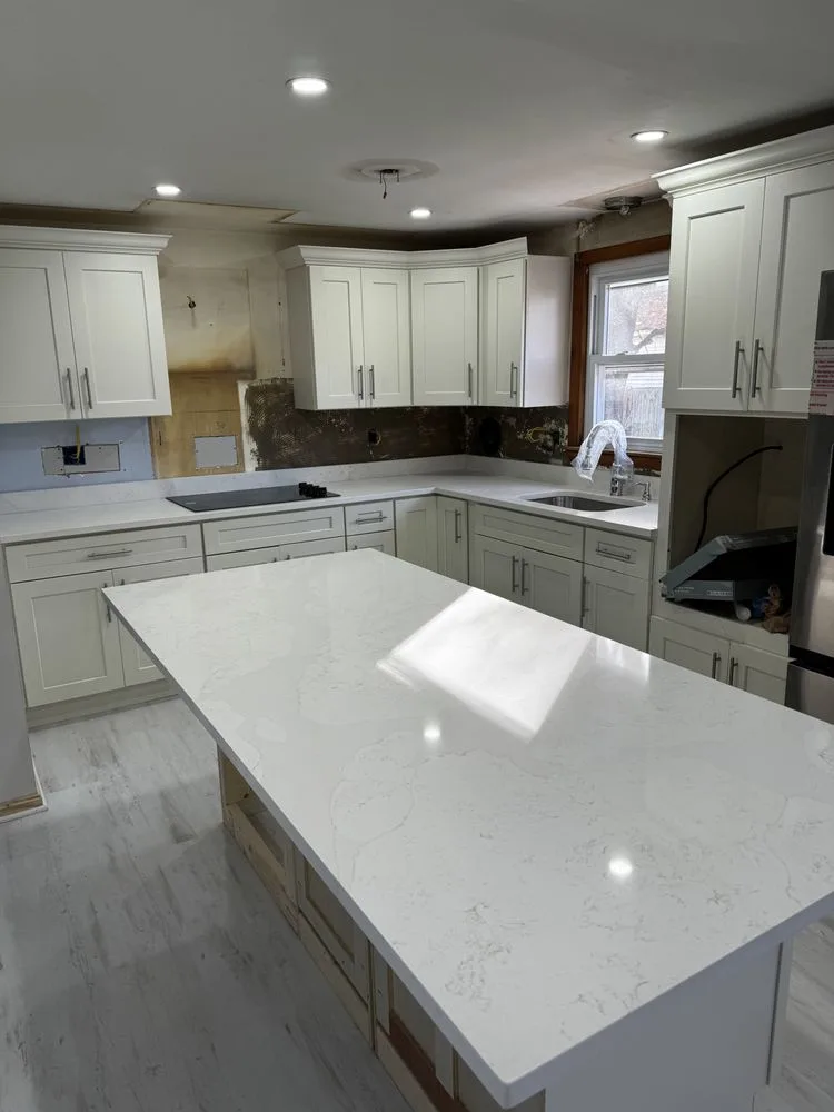 Kitchen remodeling progress showing newly installed custom cabinets, quartz countertops, and a large central island.